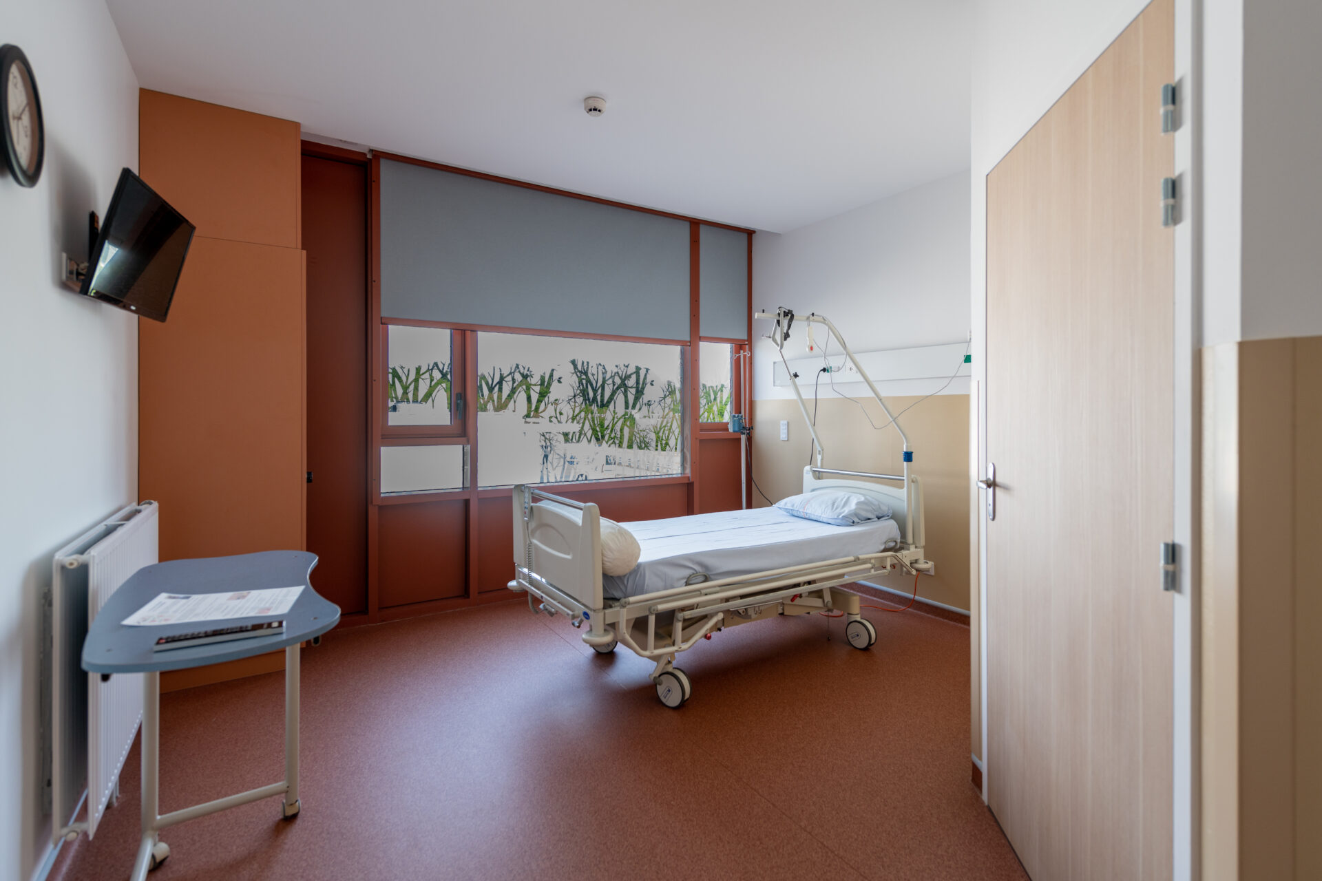 Chambre d'hôpital moderne et bien équipée du Centre Hospitalier de Douarnenez avec des équipements de soin de santé durables, conçue par l'agence d'architecture A26 pour un confort optimal des patients