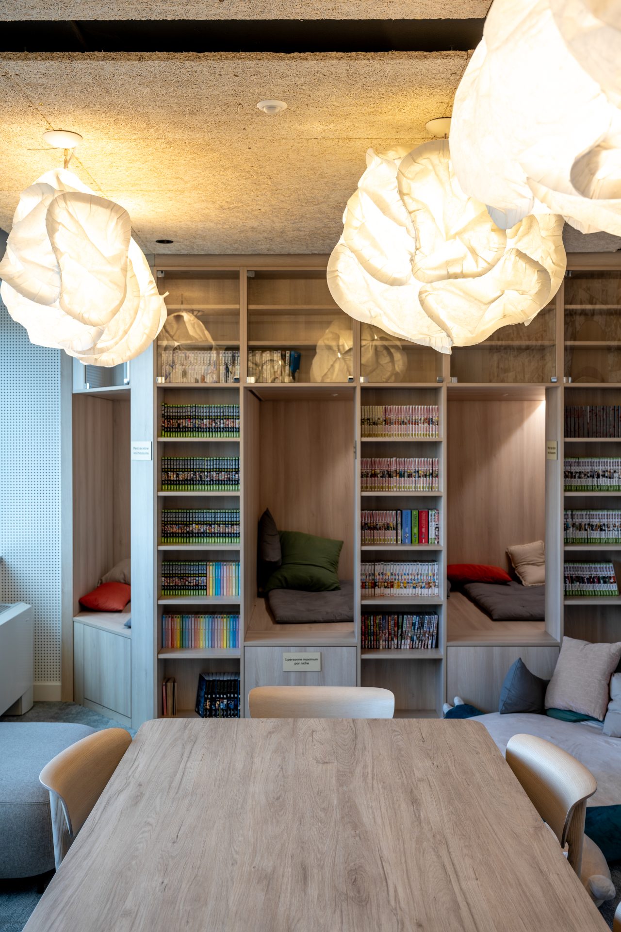 Bibliothèque étudiante moderne au sein du "Le Dojo", avec des étagères en bois et des zones de détente, reflétant la transformation d'un bureau en espace éducatif